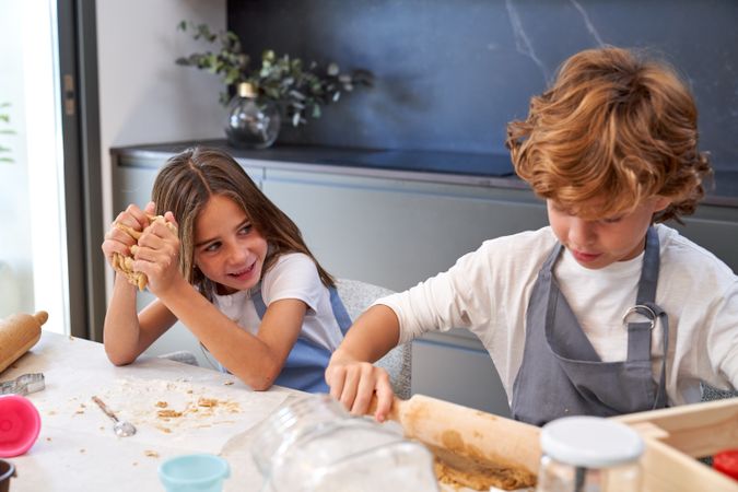 Cute happy kids rolling and kneading dough while cooking in kitc
