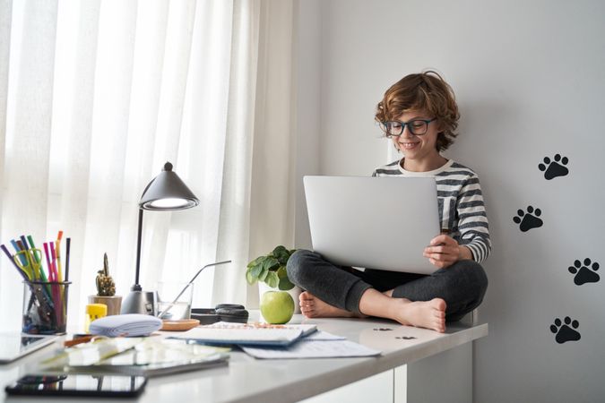 Happy barefoot boy looking at screen and using laptop at home