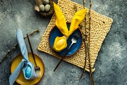 Top view of Easter holiday table setting with yellow egg decoration in bunny napkin on plate
