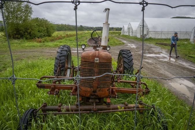 Copake, New York - May 19, 2022: Rusted tractor with female farming walking speaking on phone