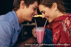 Close up of a happy couple sharing a milkshake with two straws 0L9pg5