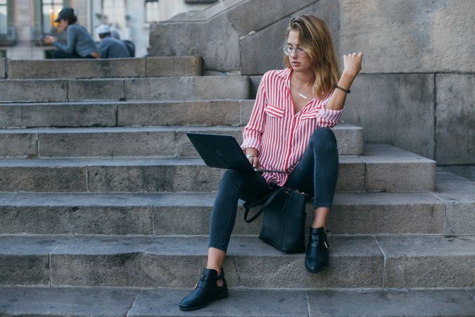 A young woman with a laptop sitting on the stairs, near the university