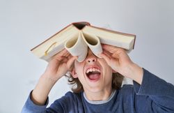 Funny boy with mouth opened looking through binoculars from book