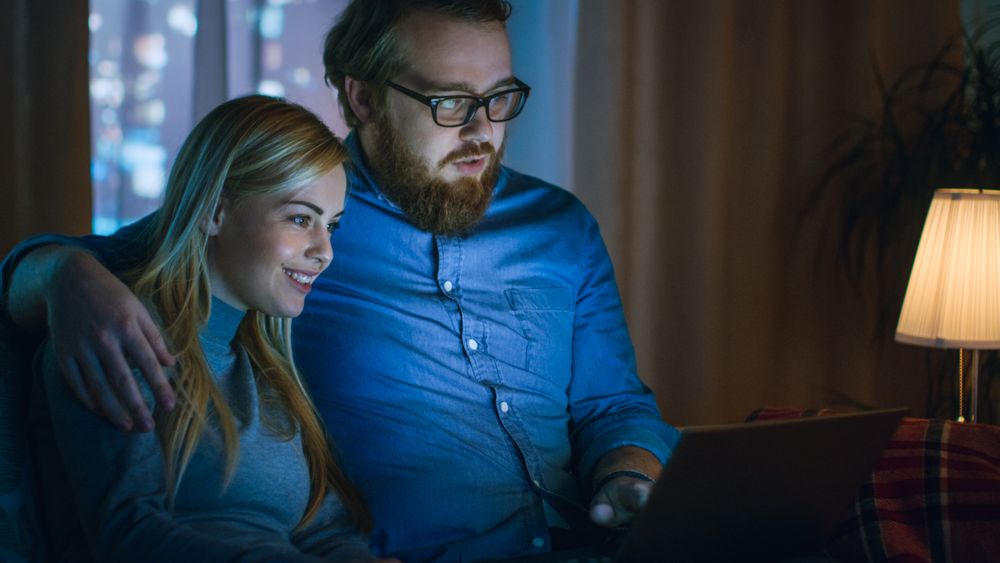 In the Evening Man and Woman are Sitting on the Sofa Watching Something on a Laptop.