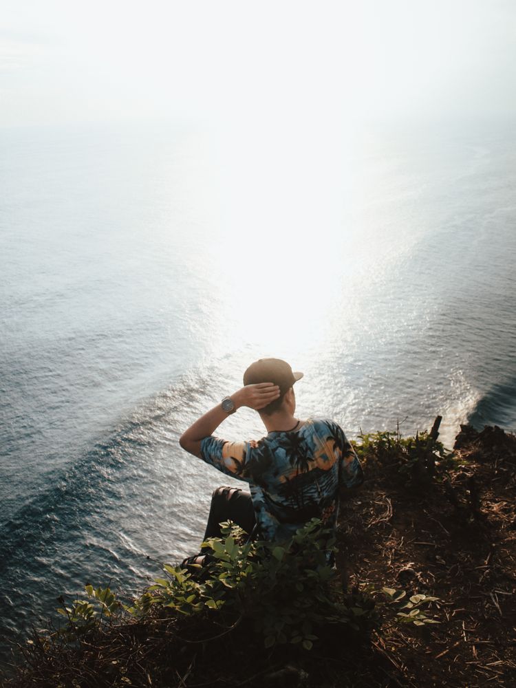 Man in floral shirt sitting on rock near beach
