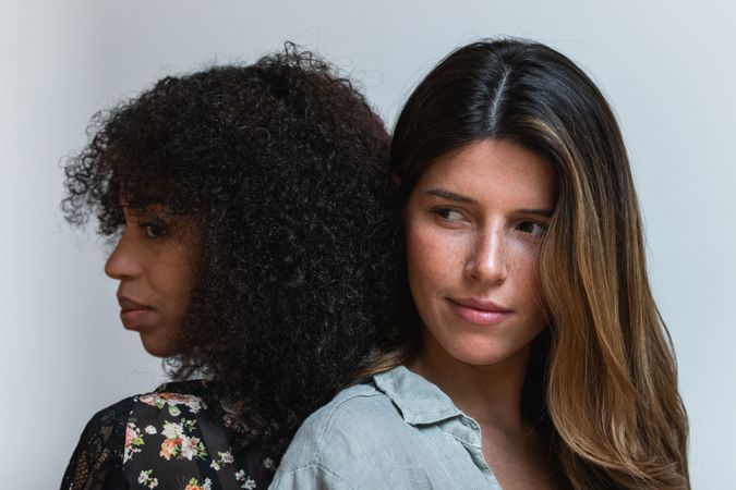 Multiracial girlfriends standing close on light background
