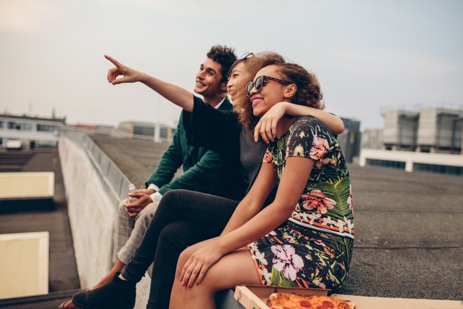 Happy young friends relaxing on rooftop, with woman pointing at something interesting