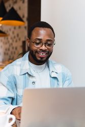 Delighted Black man with coffee browsing laptop