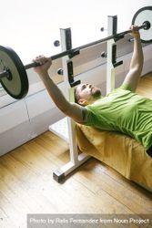 Looking at down at man in green t-shirt lifting heavy bar exercising chest bxpBXb
