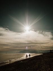 Couple walking on beach against sundown