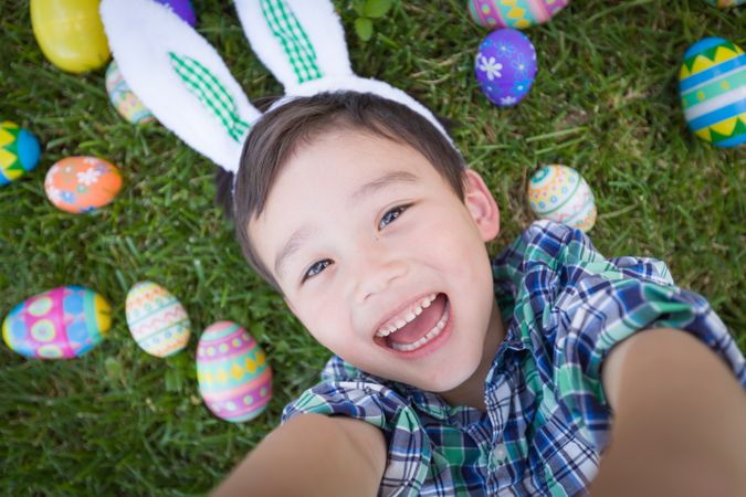 Happy Boy Outside Wearing Rabbit Ears Playing with Easter Eggs