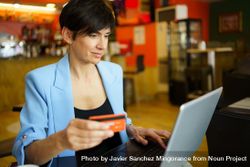 Female in trendy blue jacket sitting in cafe shopping on laptop with credit card 4BadWX