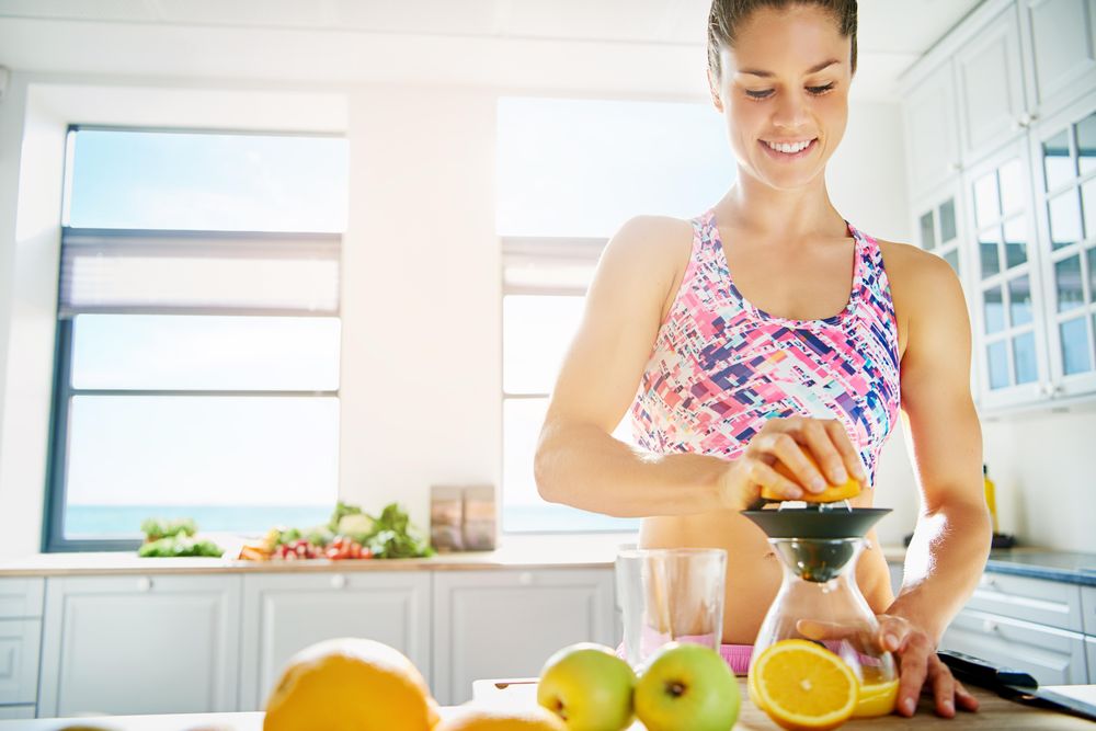 Fit woman in sports bra juicing an orange