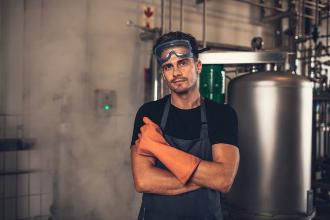 Portrait of male brewer wearing work clothing standing beside metal tank