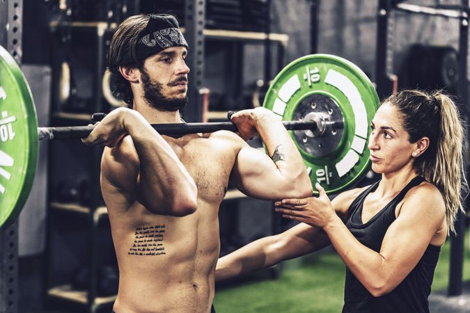 Muscular man lifting heavy weight in sport club and listening to personal trainer