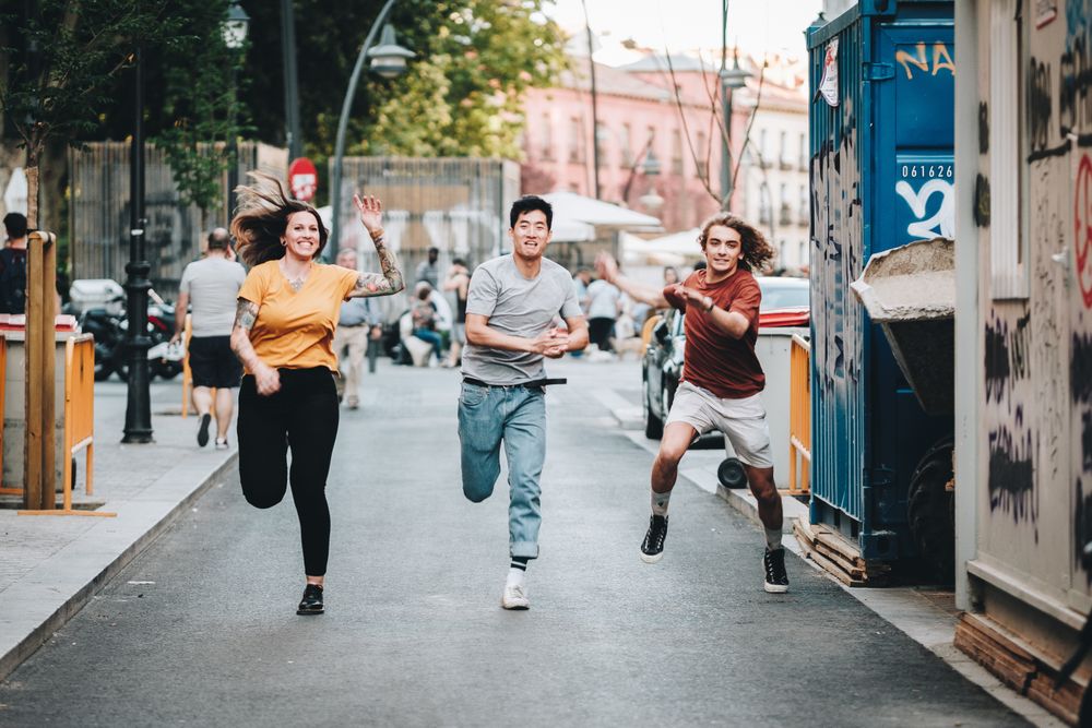 Funny multiracial friends having fun and running along city street