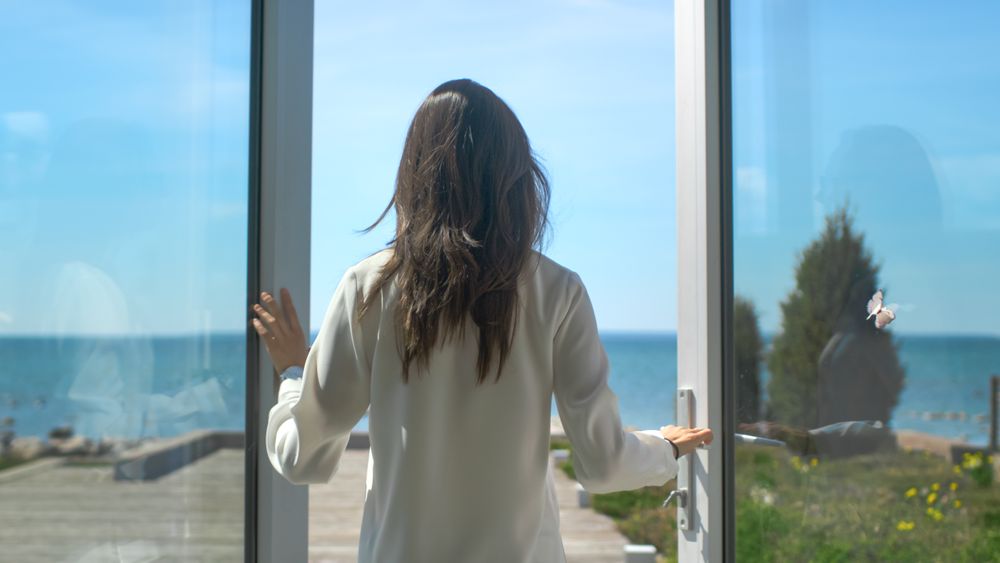 Shot of a Brunette with Loose Hair Opening Doors of the Balcony and Walking onto Sunny Terrace with Seaside View.