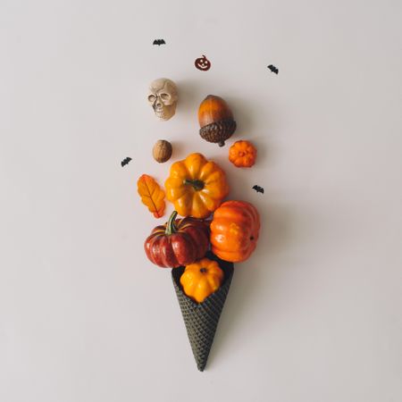Pumpkins and halloween decorations in dark ice cream cone on light background