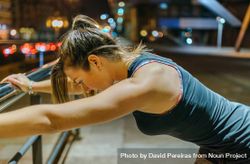 Portrait of female young athlete stretching using banister after training at night in city 4Azmvm