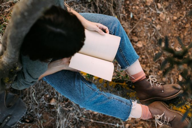 Above view of woman in jeans  and boots outside with book
