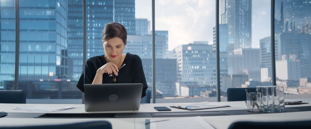 Portrait of Young Successful White Businesswoman Sitting at Desk Working on Laptop Computer in City Office.