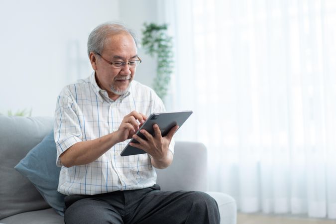 Older male sitting at home with digital tablet