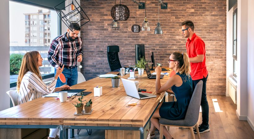 Colleagues talking in office while two of them having fun playing ping pong over coworking table