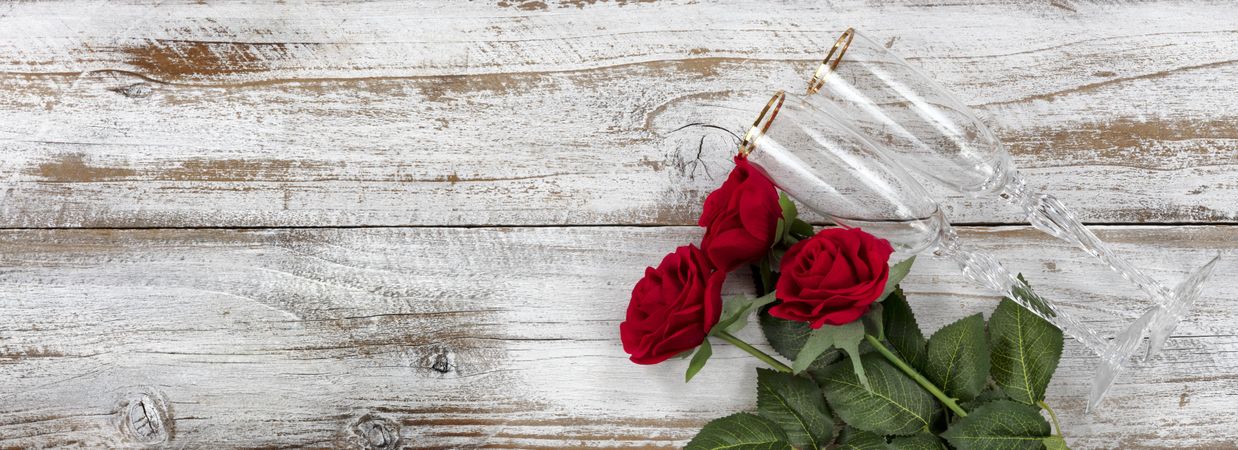 Happy Valentine’s Day celebration with red roses and drinking glasses on weathered wood
