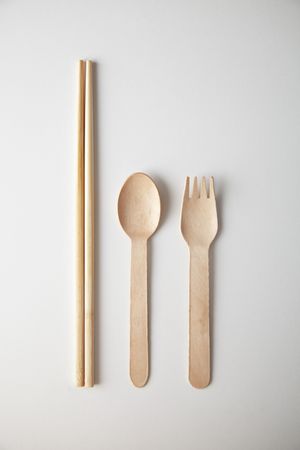 Chopsticks, spoon and fork on bright background, vertical