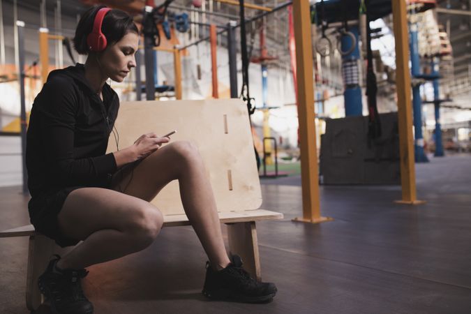 Woman with headphones and device sitting in gym
