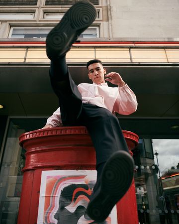 Stylish young man sitting on red mail box