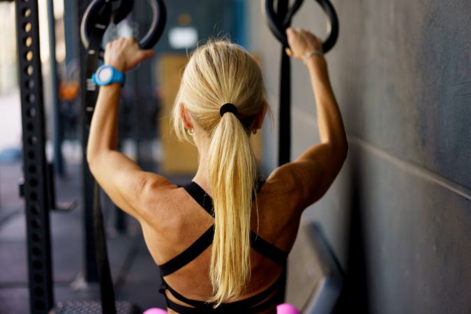 Back of blonde woman using gymnastic bars in gym
