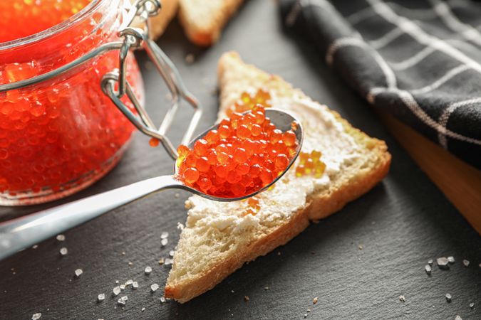 Composition with caviar in glass jar, bread, spoon, towel and cutting board, space for text