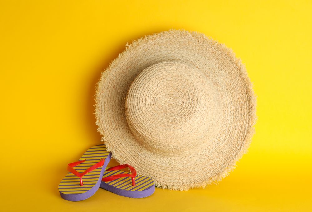 Straw hat and flip flops on color background, space for text. Summer accessories