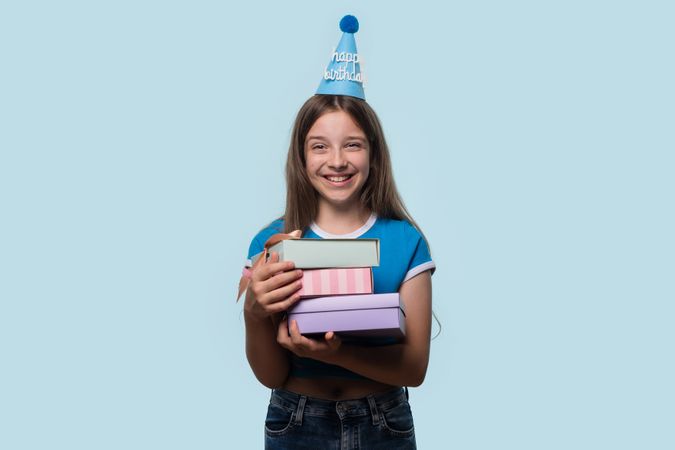 Girl holding stack of wrapped gifts, celebrating birthday.