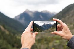 Crop traveler taking photo of mountains on smartphone