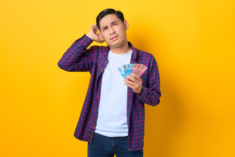 Man scratching head and holding cash
