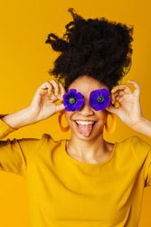 Joking Black woman sticking her tongue out with two purple flowers over her eyes