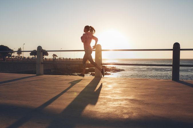 Outdoor shot of young woman running on seaside promenade
