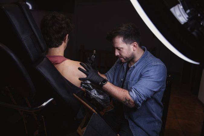 Master doing tattoo on forearm of male customer