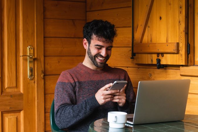 Cheerful man browsing on smartphone and working on terrace