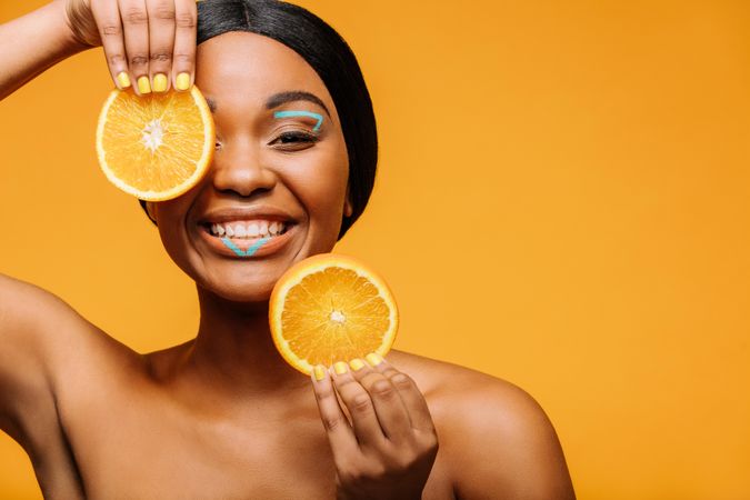 Smiling woman with vivid makeup and orange slices in hand
