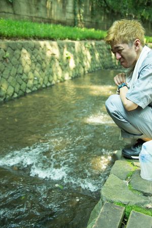 Exhausted man in work suit crouching beside stream river