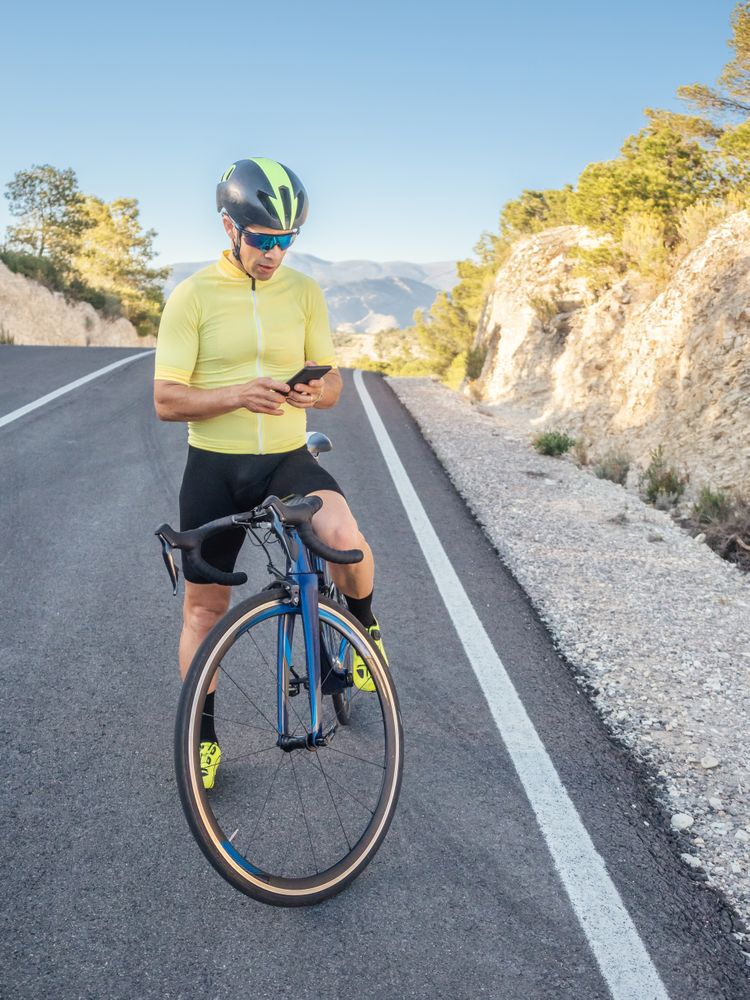 healthy man with smartphone after cycling in a mountain road in a sunny day