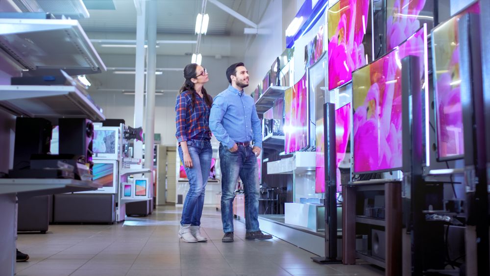 In the Electronics Store Young Couple is Choosing Which a New Model of 4K TV's is Best for Their Home and Budget.