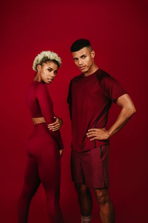 Black athletic couple standing together on maroon background