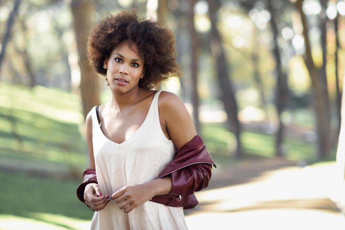 Woman standing in front of trees with red leather jacket off her shoulders
