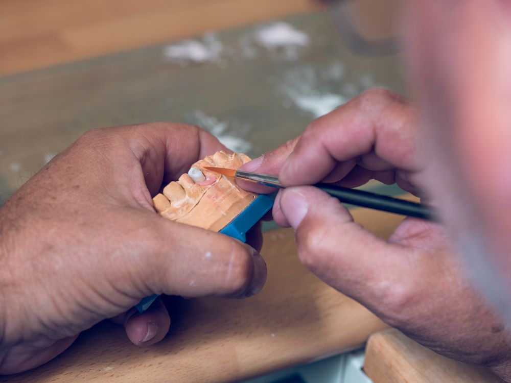 Crop man dental technician applying ceramic on denture