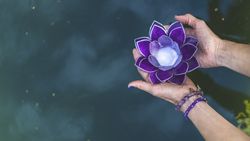 Top angle view of hands holding a purple glass lotus over water. Yoga and meditation concept. Copy space