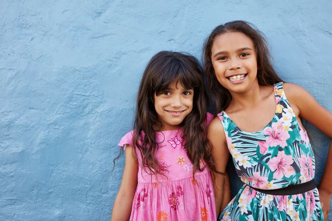 Portrait of two little girls standing together against blue background